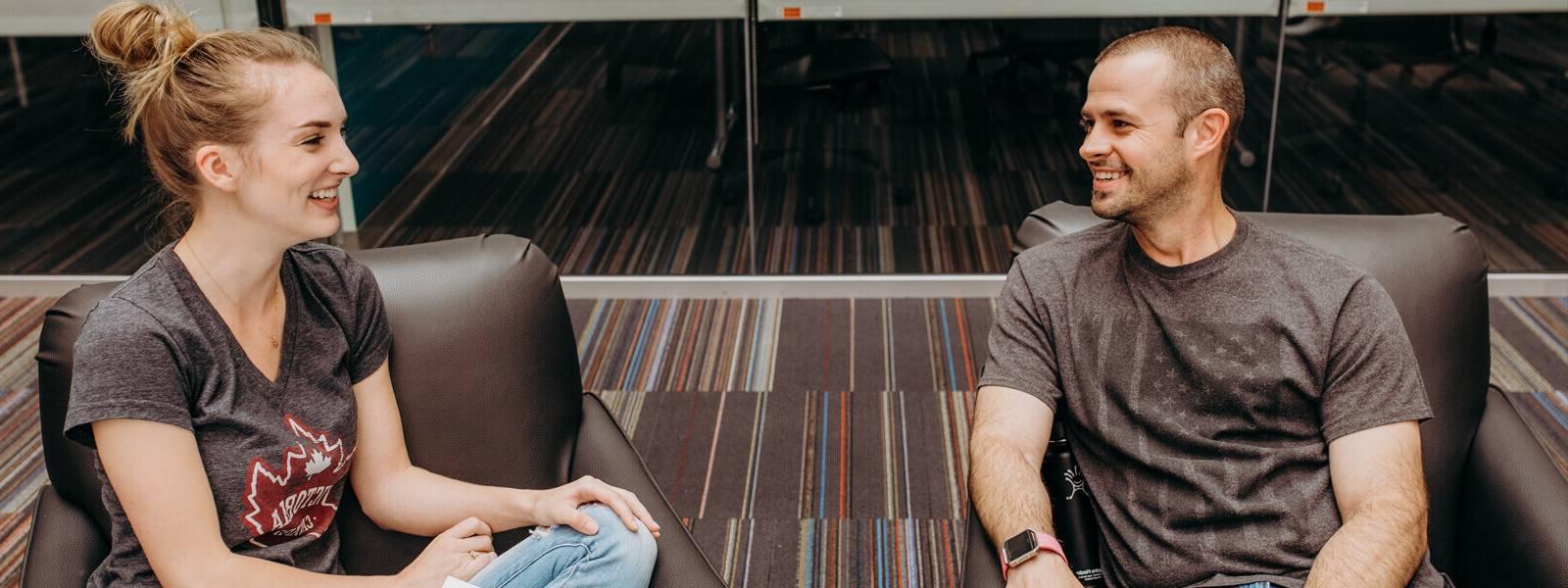 Two students sitting in chairs talking and smiling